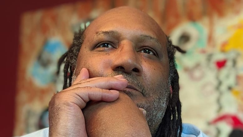Lewis Gordon is Afro-Jewish. He has long dreadlocks and in this photo he is wearing a blue shirt and his elbows are on a table with his arms up and hands near his face. You can see his watch and gold bracelets.