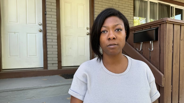 A woman stands in front of a house door and porch.