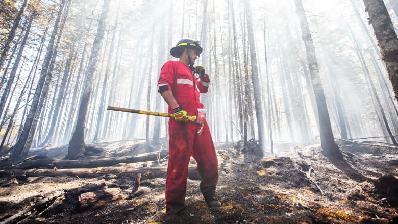 A man in a red jumpsuit stands in the woods with an axe in the hands.