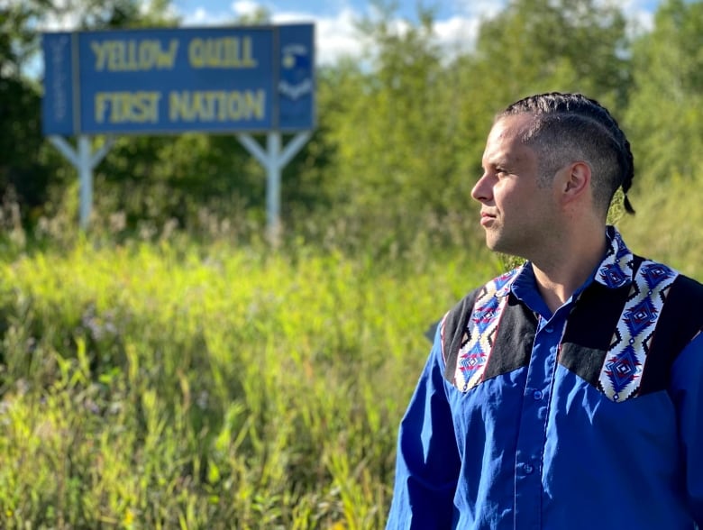 An Indigenous man stands outside looking to the left.