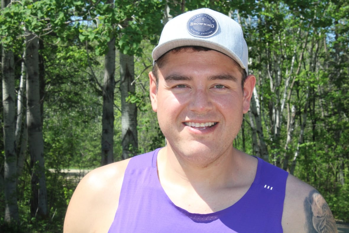 An Indigenous man wears a white hat and a purple tank top