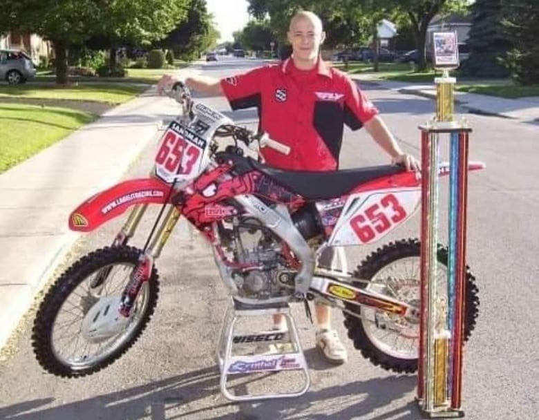 A man standing with a dirt bike and a trophy.