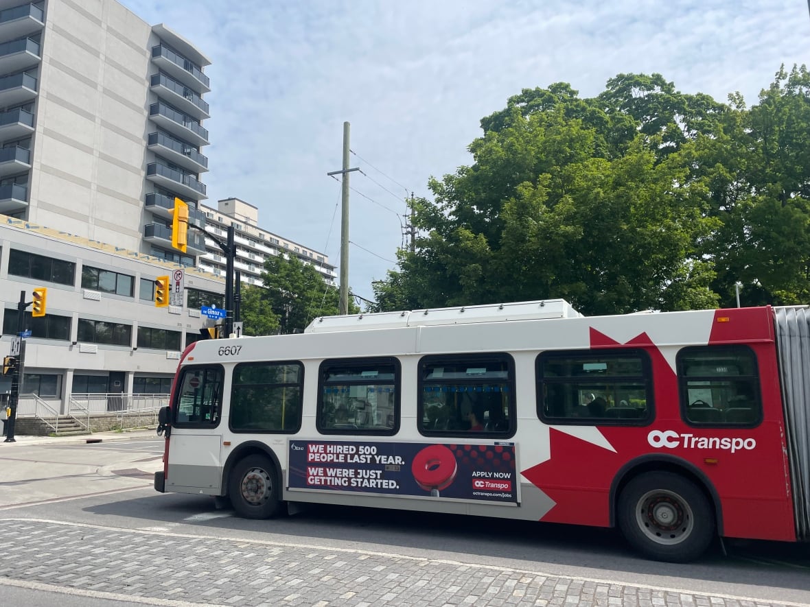 A red and white bus with an ad on the side promoting jobs with the bus company.