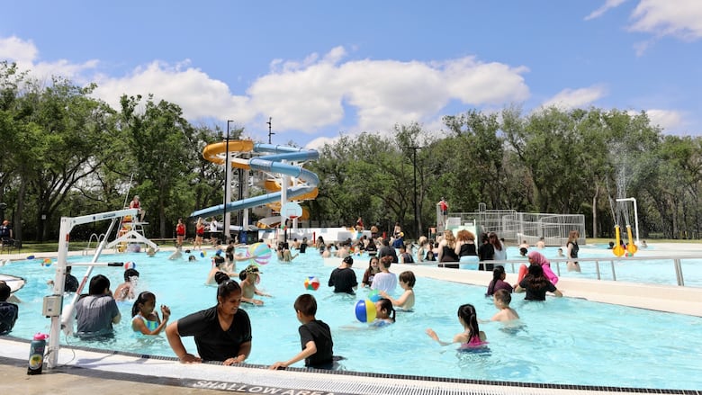 Children enjoy a outdoor pool. A pair of waterslides are in the background.