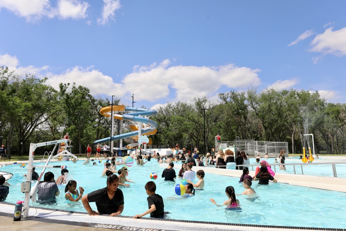 Children enjoy a outdoor pool. A pair of waterslides are in the background.
