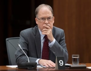 A man in a grey suit sits in front of a microphone.
