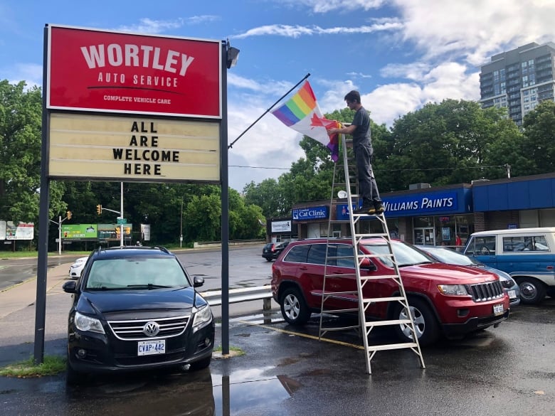 Worker on ladder adjusts pride flag 