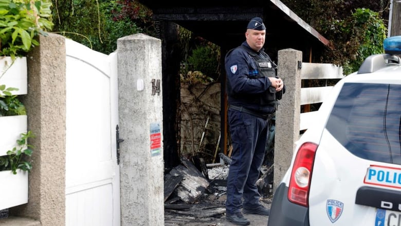 A police officer stands in front of the smashed gate of a home.