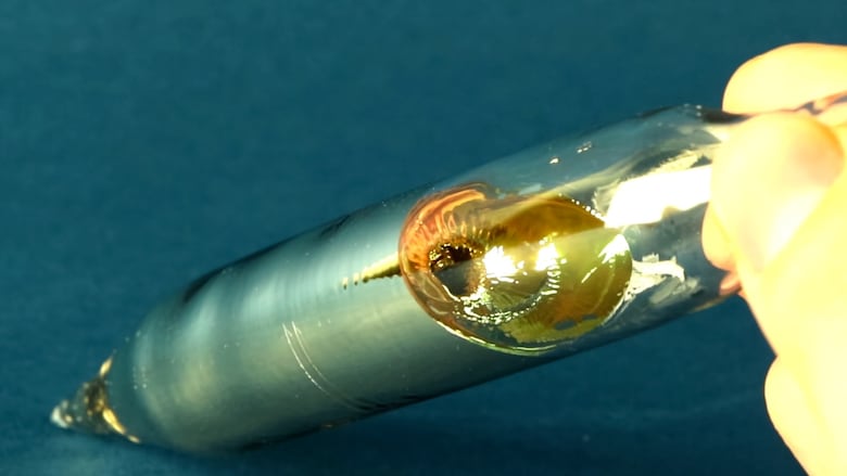 A gloved hand holds a glass tube with a golden, metallic liquid inside.