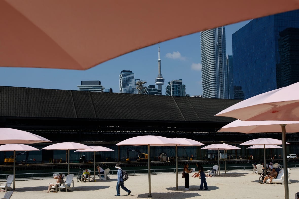 People at sugar beach with umbrellas for shade and CN tower in the background.