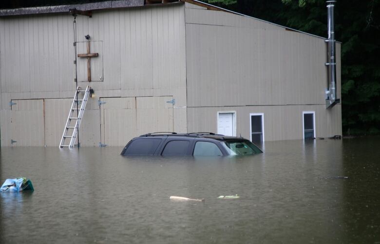 A van is shown submerged up to its windows next to a building as heavy flooding is shown.