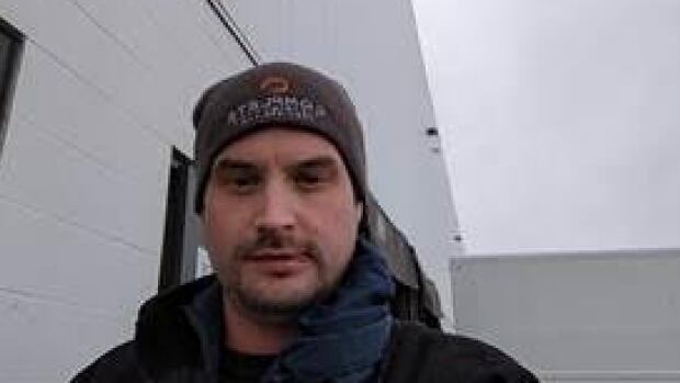 Aarron Kowalchuk, 34, was arrested by the ALERT Internet Child Exploitation (ICE) Unit in Edmonton last month. A man with a grey beanie and facial hair poses for a selfie. He appears to be outside, near a large white building.