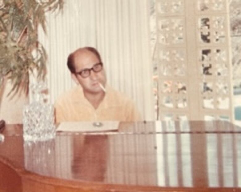 A bald man smoking a cigarette and playing the piano. 