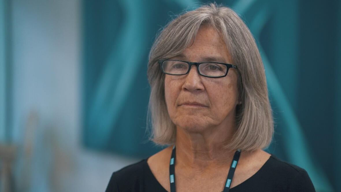 A woman with classes looks off camera.