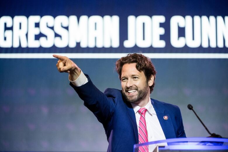 A man in a suit on stage pointing.
