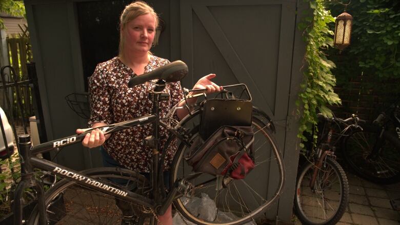 Woman standing holding the remains of her broken bike.