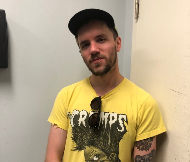 A man poses in a yellow t-shirt and hat.