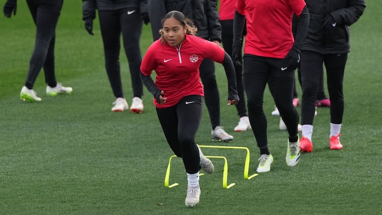 A female soccer player runs over obstacles during a training drill as teammates line up in single file awaiting their turn.