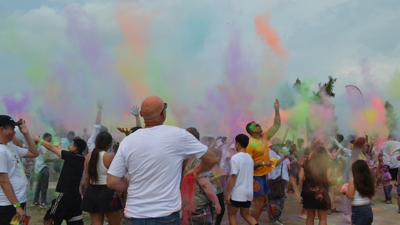 People in white shirts throw coloured powders into the sky. The ski is filled with green, orange, purple and pink powders.