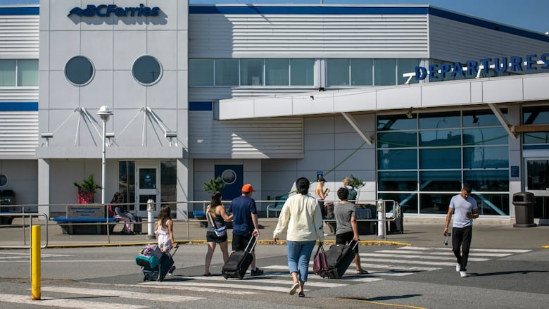 People are pictured wheeling suitcases on their way to a B.C. Ferries terminal.