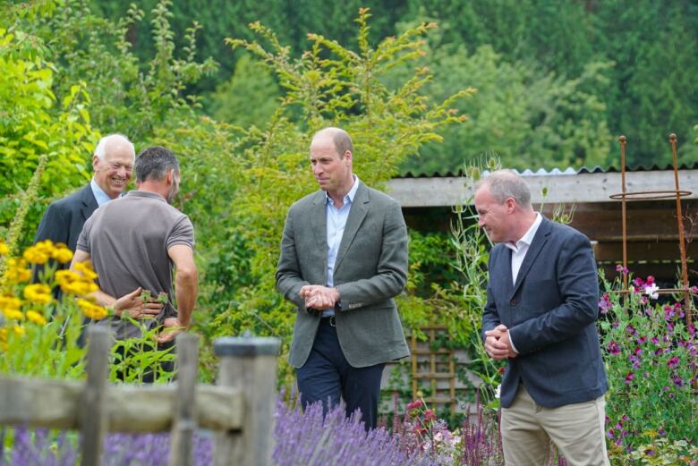 Four people smile and talk with one another in a garden.