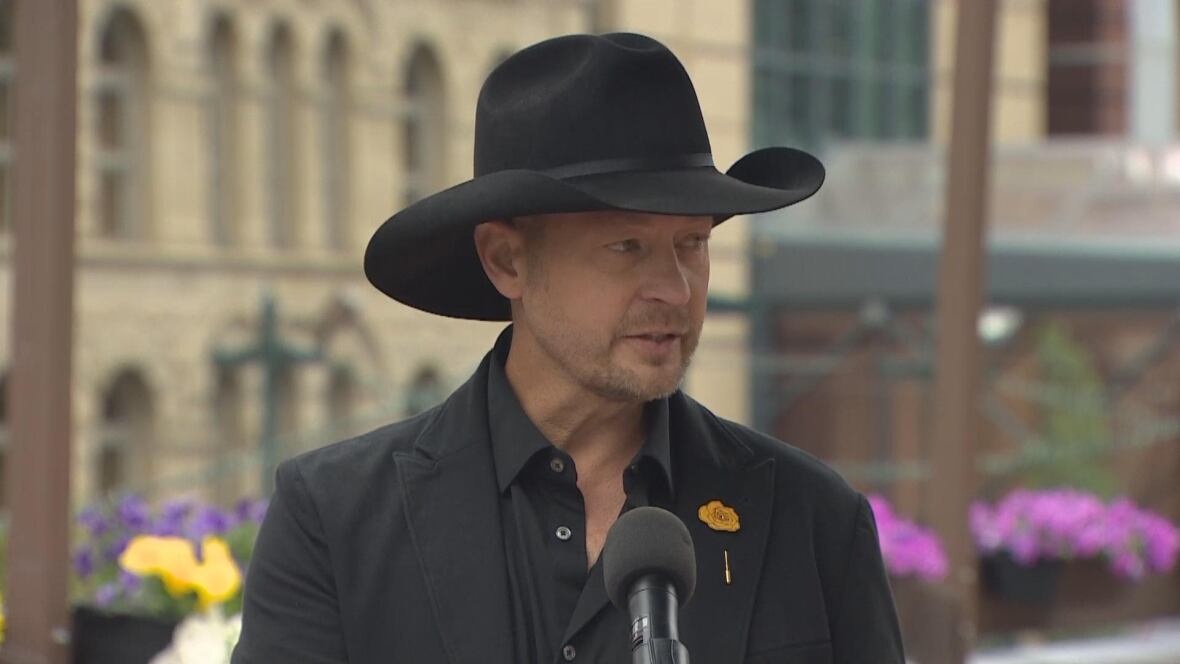 A man in a black cowboy hat speaks into a microphone. 