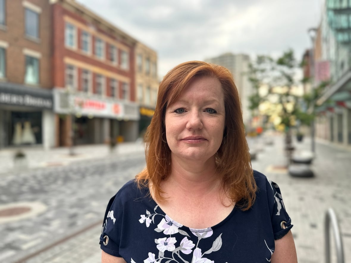 woman with red hair wears a floral shirt and stands on a city street in London