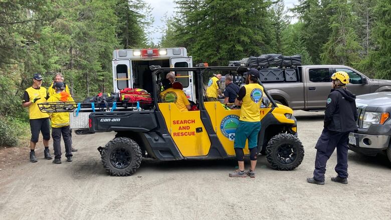 A truck named 'search and rescue' stands at the middle of a backcountry road, with several people standing around and vehicles parking around.