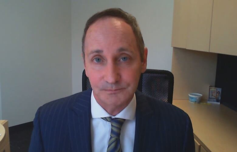 A man in a dark blue suit and white shirt stares into the camera.