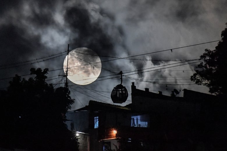 Moon rises in the sky behind a moving cable car in Caracas, Venezuela.