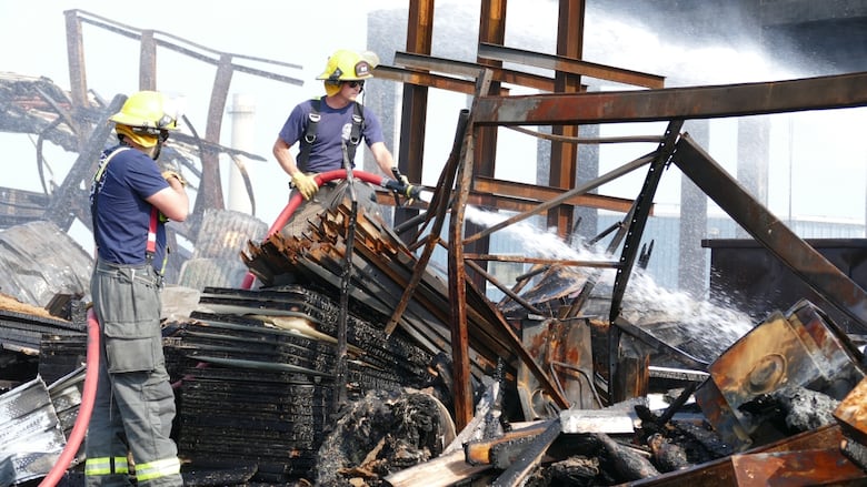 Two firefighters put out hot spots Monday after a major fire at an industrial building. 