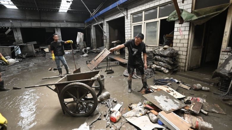 Two men clear debris from a flooded warehouse.