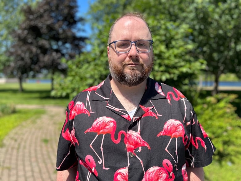 A man wearing glasses and a shirt with flamingos stands outside on a summer day