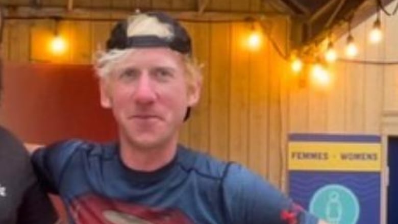 A man with blond hair wearing a backward black ball cap and Superman shirt.