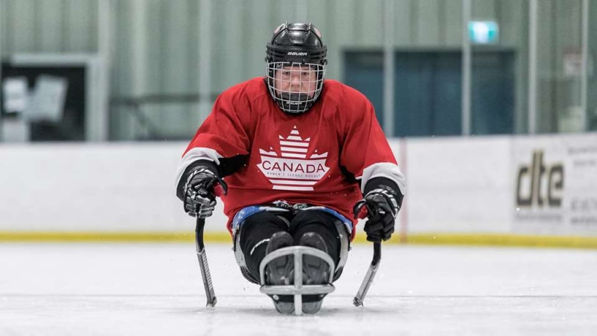 A female Para ice hockey player wearing red Canadian gear is seen in the sled on the ice.