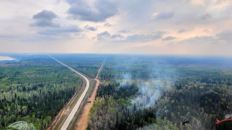 Aerial shot with a rural road surround by forest - the forest on the right side of the road is smoking.