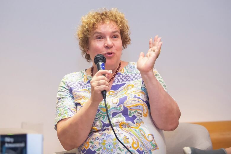 A woman in a paisley top speaks into a microphone.