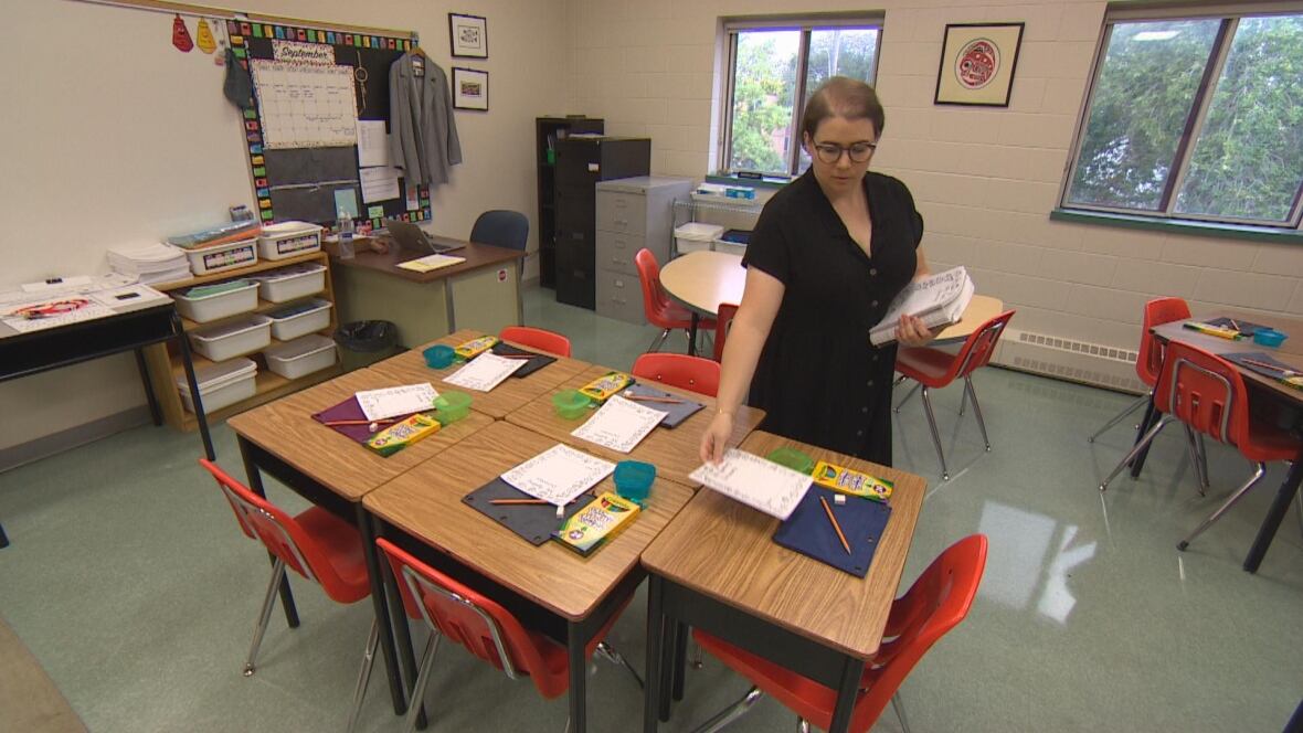 A teacher wearing a black outfit places assignments down on students' desks.