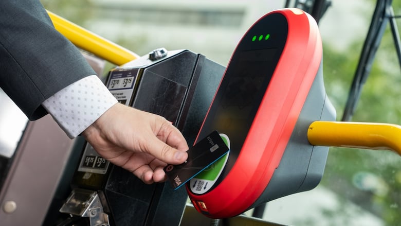 A person taps a credit card on a red pay station on a bus.