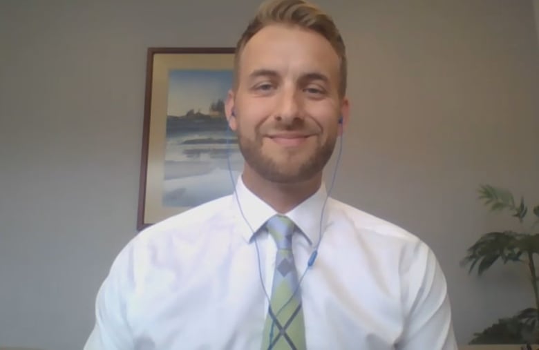 A man in a green tie and white dress shirt smiles in front of the camera on a Zoom call.