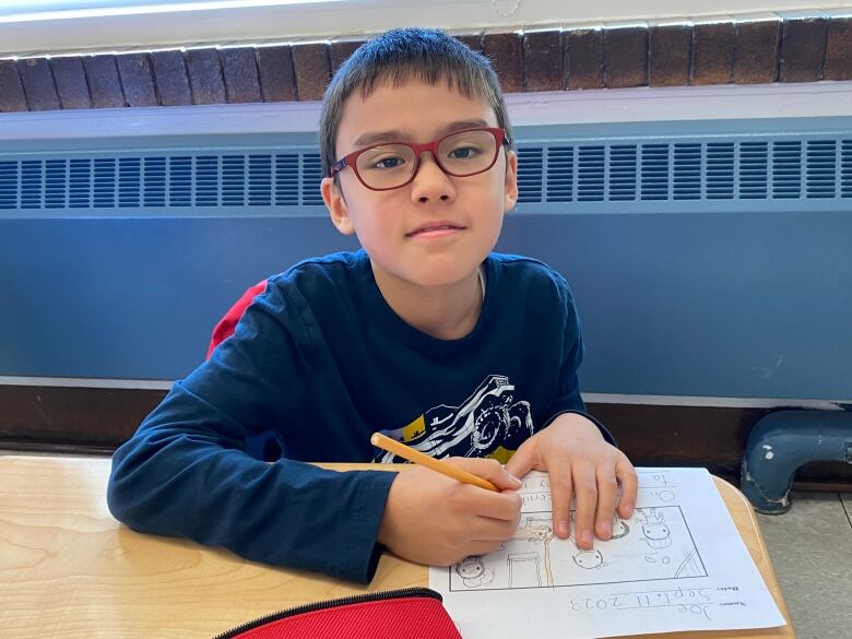 A young boy wearing glasses smiles at the camera.