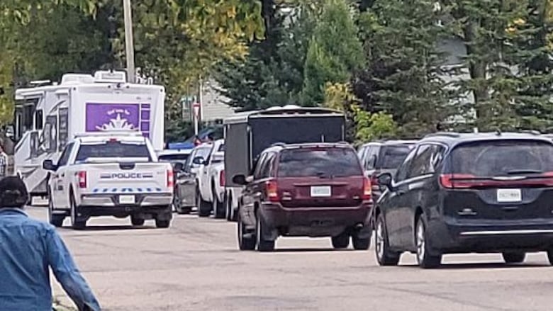 Several vehicles are driving through a suburban street, including an RV with a purple flag followed by an RCMP truck.