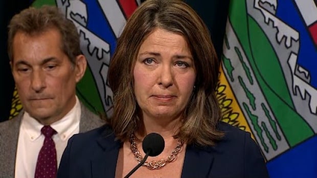 Alberta's premier is seen answering questions astatine  a podium.