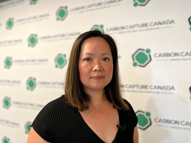 A woman in a black dress poses in front of a "Carbon Capture Canada" poster at the Edmonton Convention Centre.