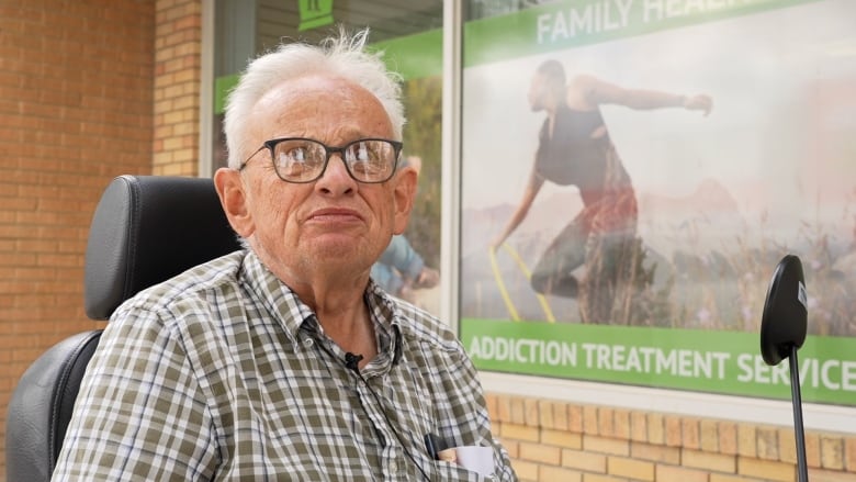 An elderly man with grey hair wearing glasses sitting in a mobility scooter