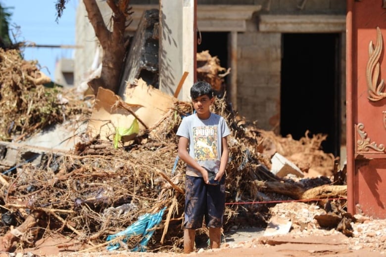 A boy stands next to debris from flooding.