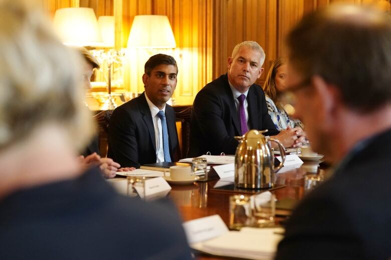 Two men sit at a crowded conference table. 