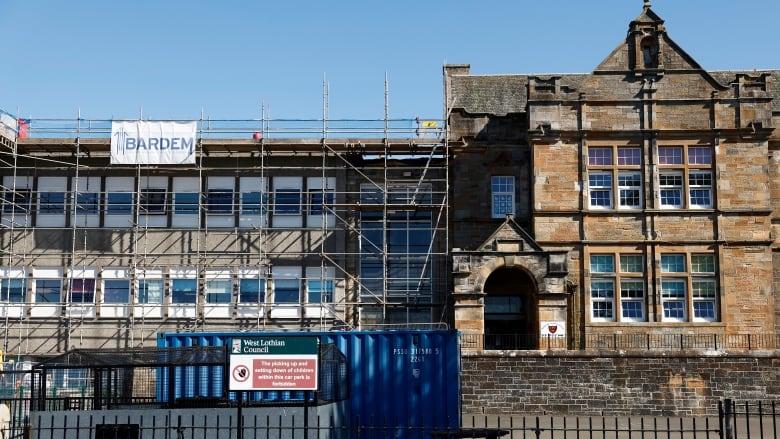 The concrete exterior of a school building is covered in scaffolding. 