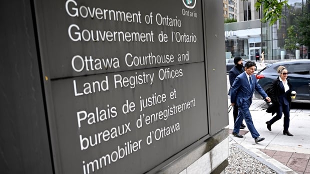 Three people walk past a sign for a provincial courthouse in a city.