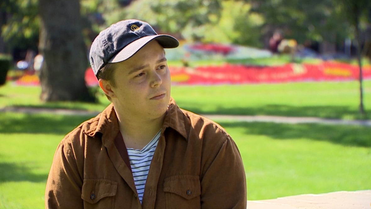 A person wearing a hat and button down shirt looks off camera during an interview. 